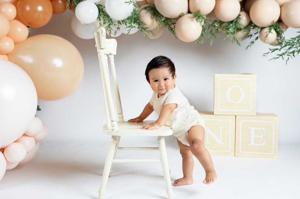 One year old baby standing by chair while we take portraits before cake smash